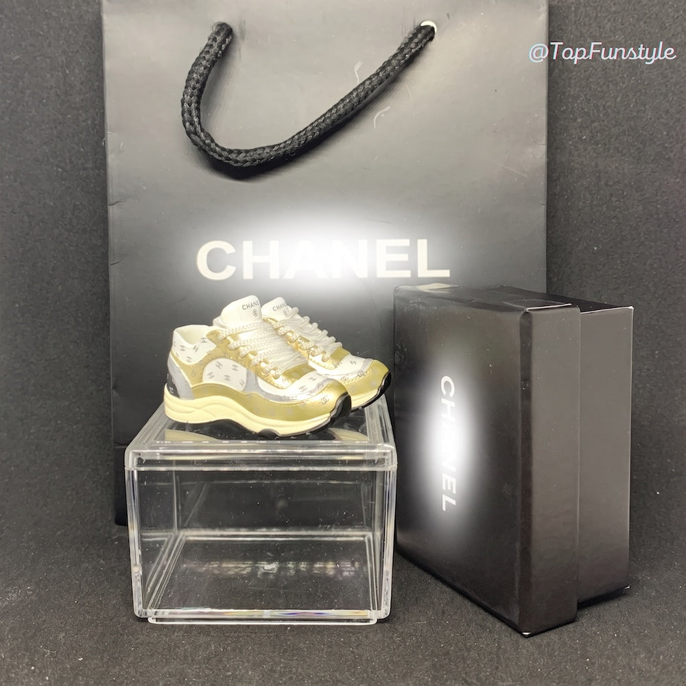 Mini sneakers Chanel CC doré sur vitrine avec boîte et sac - vue d'ensemble kit