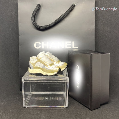 Mini sneakers Chanel CC doré sur vitrine avec boîte et sac - vue d'ensemble kit