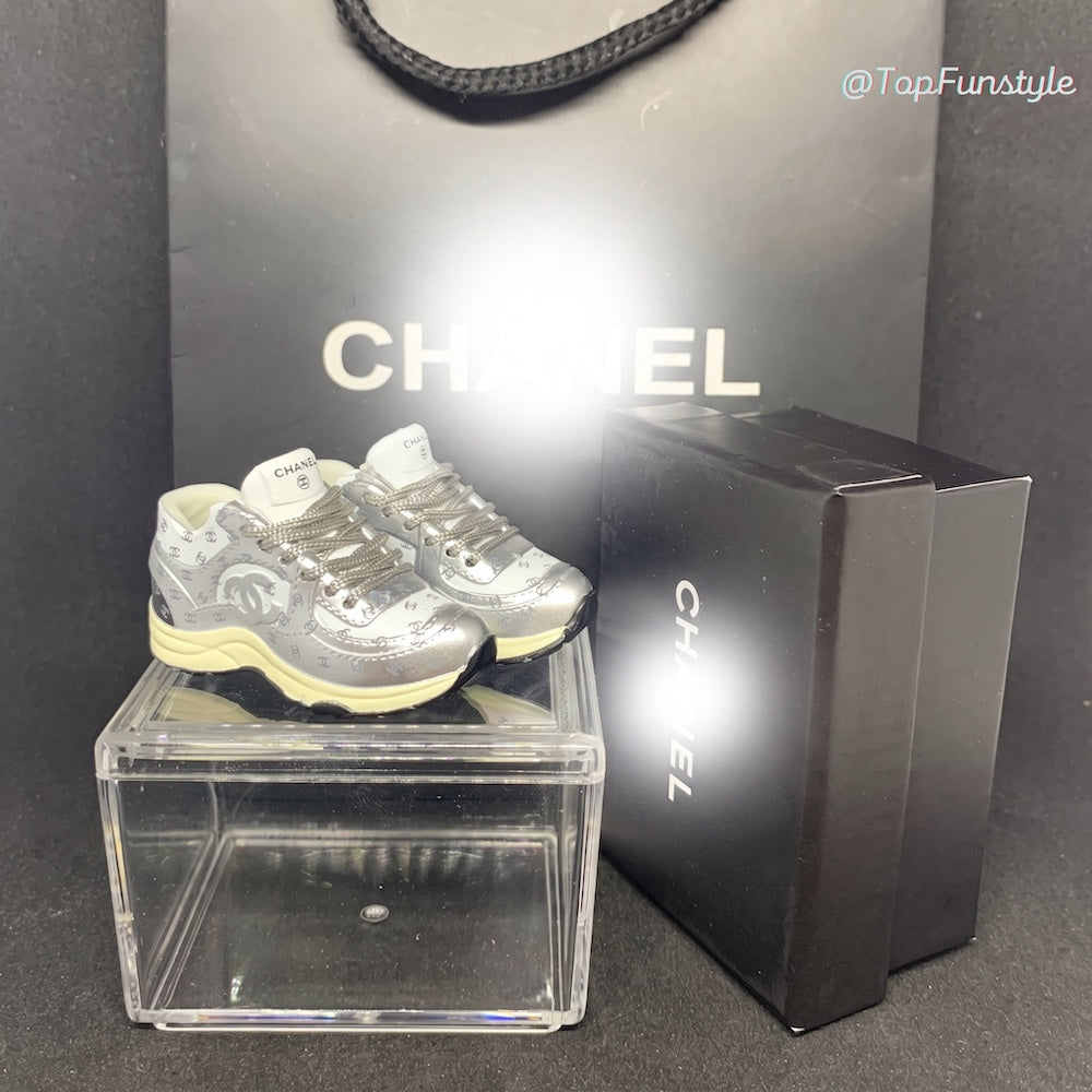 Mini sneakers Chanel CC argenté sur vitrine avec boîte et sac - vue d'ensemble kit