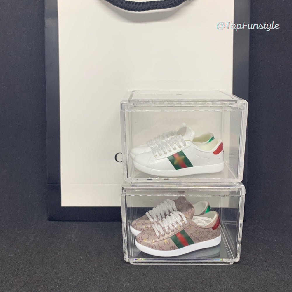 Mini baskets Ace abeille blanches et GG beige rosé dans deux vitrines superposées, modèles vendus séparément.