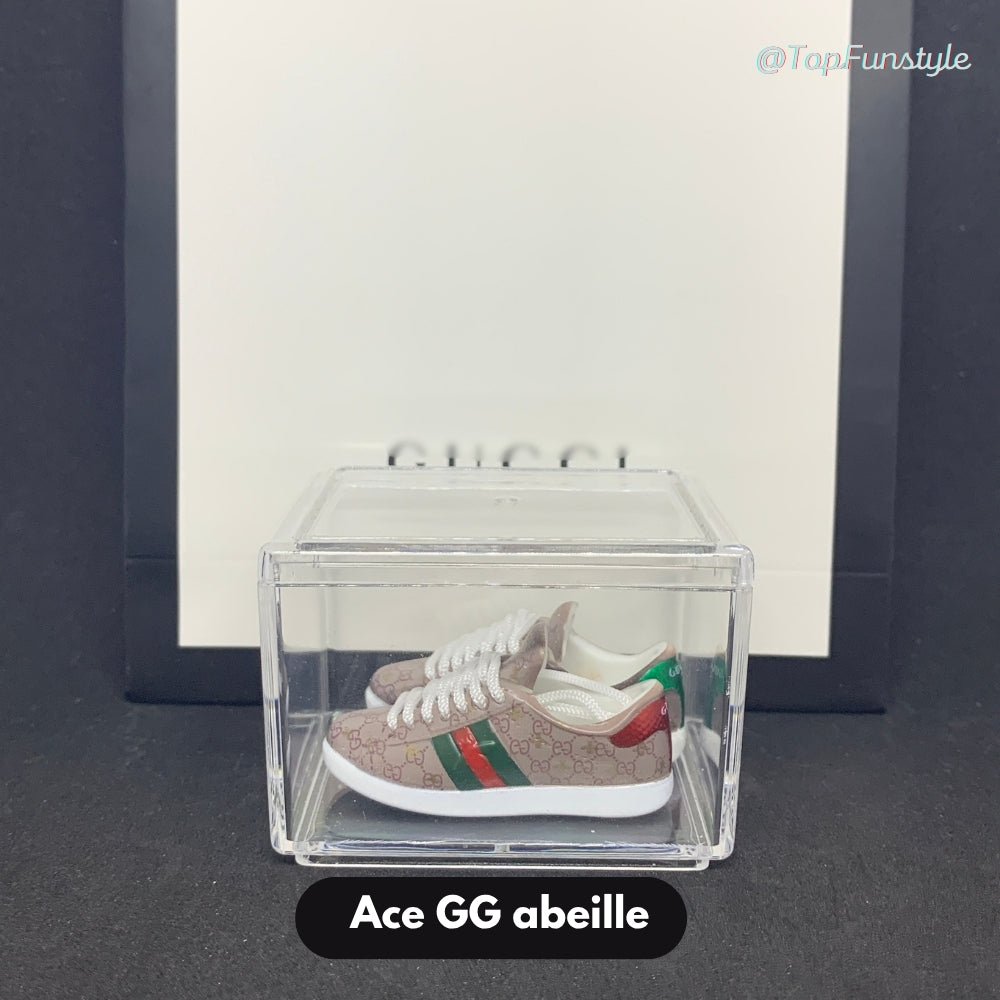 Paire de mini baskets Ace GG abeille beige rosé inspirées de Gucci, exposée dans une vitrine transparente.
