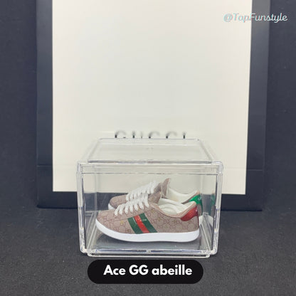 Paire de mini baskets Ace GG abeille beige rosé inspirées de Gucci, exposée dans une vitrine transparente.