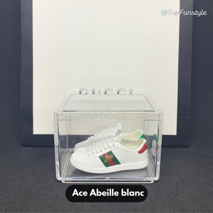 Paire de mini baskets Ace abeille blanches inspirées de Gucci, exposée dans une vitrine transparente.