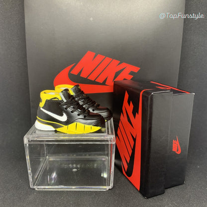Mini sneakers Kobe 1 Del Sol noir et jaune posées sur la vitrine, boîte miniature à droite