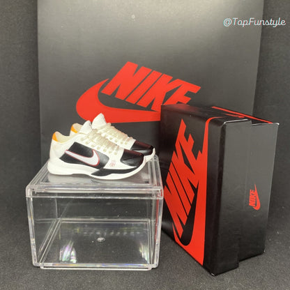 Mini sneakers Kobe 5 Bruce Lee Alternate blanc, noir et rouge posées sur la vitrine, boîte miniature à côté