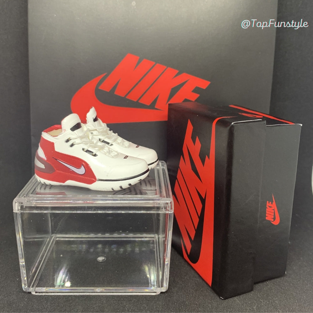 Mini sneakers LeBron 1 First Game blanc et rouge posées sur la vitrine, boîte miniature à droite