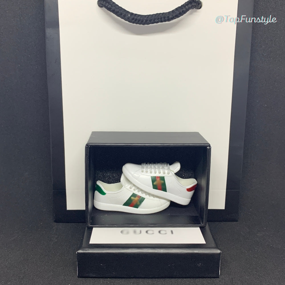 Mini baskets Ace abeille blanches dans leur boîte miniature, avec un sac cadeau en arrière-plan.