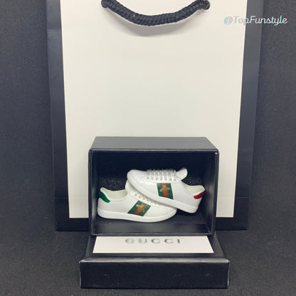 Mini baskets Ace abeille blanches dans leur boîte miniature, avec un sac cadeau en arrière-plan.