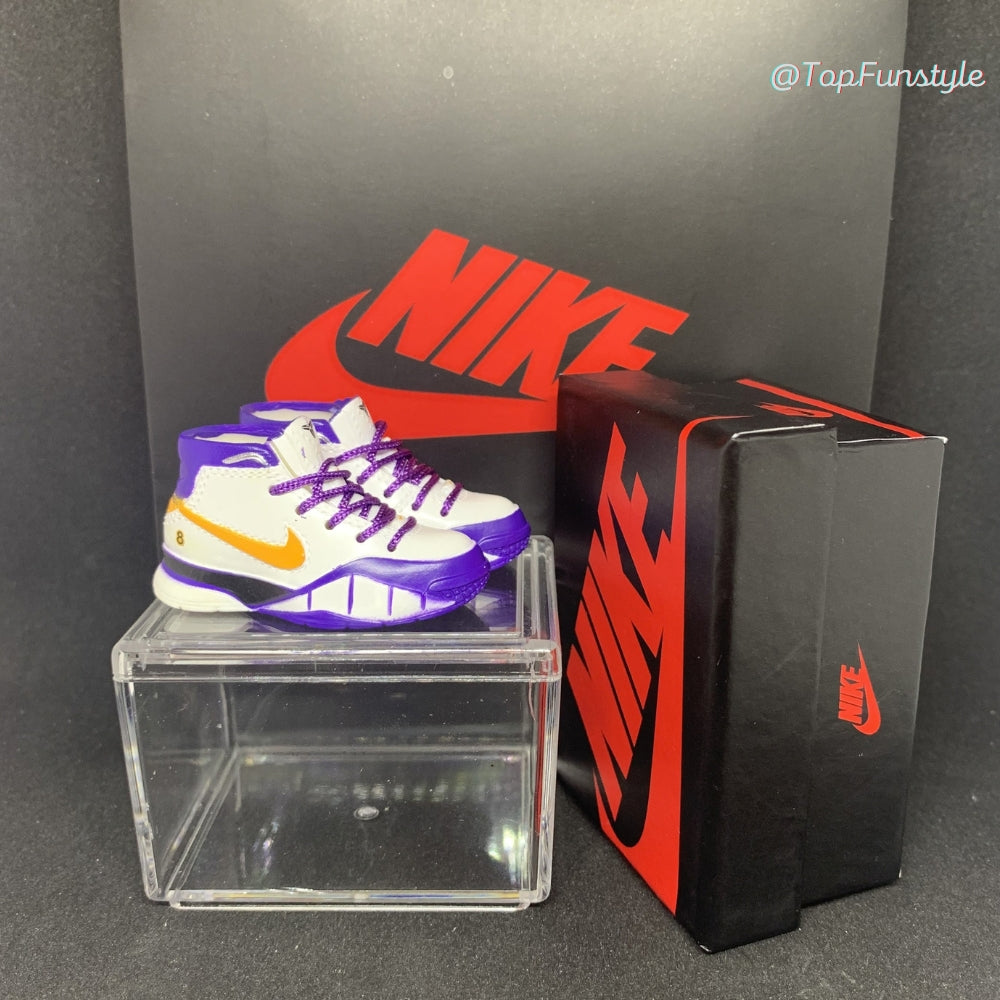 Mini sneakers Kobe 81 Points blanc, violet et or posées sur la vitrine, boîte miniature à droite